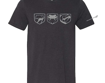 May include: A dark grey t-shirt featuring three grey snake head logos on the front. The logos are arranged horizontally and are all the same size. The logos are of the Dodge Viper.