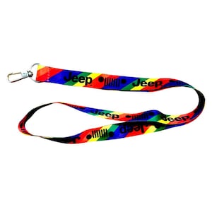 Könnte beinhalten: Ein farbenfrohes Schlüsselband mit dem Wort "Jeep" in Weiß und dem Jeep-Logo. Das Schlüsselband hat ein Regenbogen-Design mit roten, orangefarbenen, gelben, grünen, blauen und schwarzen Streifen. Es hat einen Metallverschluss.