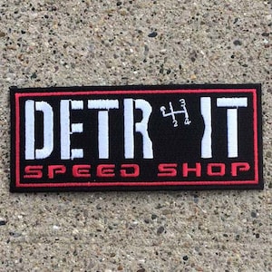 Peut inclure: Patch brodé noir et rouge avec du texte blanc qui dit "DETR*IT SPEED SHOP" avec un motif de changement de vitesse blanc au milieu.