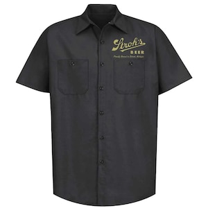 Puede incluir: Una camisa de trabajo negra de manga corta con un logotipo dorado que dice "Stroh's Beer" y "Proudly Brewed in Detroit, Michigan".