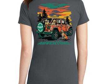 May include: Dark gray t-shirt featuring a graphic of an orange Jeep with dogs inside and out, set against a sunset backdrop. The text "Built for Adventure" is below the Jeep. The shirt is a casual wear item.
