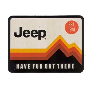 Puede incluir: Una pegatina en blanco y negro con la palabra "Jeep" en negrita, un círculo rojo con el texto "EST. 1941" y el texto "HAVE FUN OUT THERE" en blanco. La pegatina presenta una cordillera estilizada con rayas naranjas, amarillas y marrones.