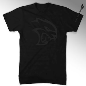 May include: Black t-shirt with a gray Dodge Challenger SRT Hellcat logo on the front and "Dodge" printed on the right sleeve.