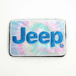 Puede incluir: Un parche bordado azul con el logotipo "Jeep" sobre un fondo blanco con un patrón tie-dye en rosa, azul y verde.