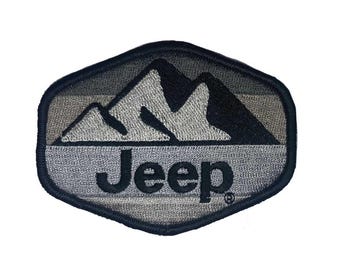 Op de afbeelding: Een geborduurde patch in zwart en grijs met een bergketen en het woord "Jeep" in zwarte letters.
