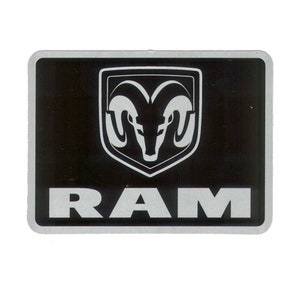 Könnte beinhalten: Rechteckiges schwarz-silbernes Emblem mit dem RAM-Logo. Das Logo ist ein weißer Widderkopf in einem Schild. Das Wort "RAM" ist in silbernen Blockbuchstaben darunter gedruckt.