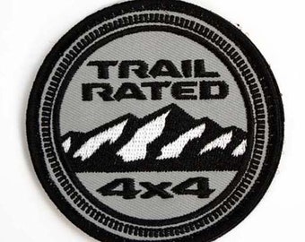 May include: A gray and black embroidered patch with the text "Trail Rated 4x4" and a stylized mountain range.