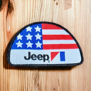 May include: A semi-circular patch featuring the American flag design with red and white stripes and white stars on a blue background. The word "Jeep" is embroidered in black below the flag design. The patch has a black border.