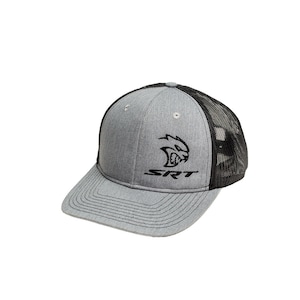 Puede incluir: Una gorra de camionero gris y negra con un logotipo SRT bordado en negro y una cabeza de animal bordada en negro y blanco.