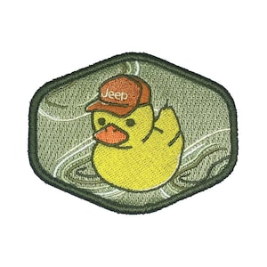 Peut inclure: Un patch brodé vert et blanc représentant un canard en caoutchouc jaune portant une casquette de baseball rouge et blanche avec le mot "Jeep" dessus.
