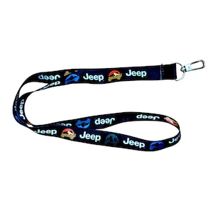Könnte beinhalten: Schwarzes Schlüsselband mit dem Wort "Jeep" in Weiß und Jeep-Grafiken in Rot, Blau und Gelb. Es hat einen Metallverschluss. Das Schlüsselband ist zum Befestigen von Schlüsseln oder einem Ausweis gedacht.