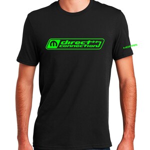 Pode incluir: Camiseta preta com um logotipo verde "Direct Connection" e um logotipo verde "Mopar" na manga direita.