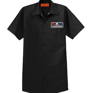Puede incluir: Camisa de trabajo negra de manga corta con cierre de botones y dos bolsillos en el pecho. La camisa tiene un parche con el logotipo de Mopar en el bolsillo derecho del pecho.