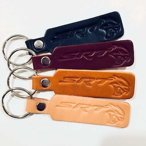 May include: Four leather keychains with a silver key ring. Each keychain has the word "SRT" and a stylized image of a viper. The keychains are in black, burgundy, brown, and tan.