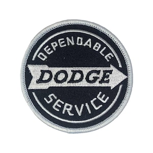 Op de afbeelding: Een ronde patch met de tekst "DEPENDABLE DODGE SERVICE" in witte letters op een zwarte achtergrond. Een witte pijl wijst naar het woord "DODGE". De patch heeft een witte rand.