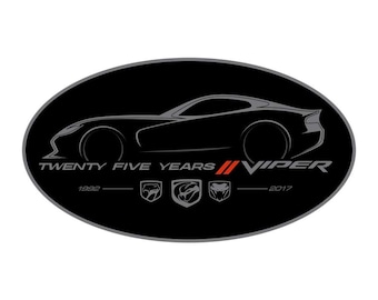 May include: A black and grey oval sticker with a silhouette of a Dodge Viper car. The text "TWENTY FIVE YEARS" and "VIPER" are printed in grey. The years 1992 and 2017 are printed in grey below the text. Three grey Viper logos are printed below the text.