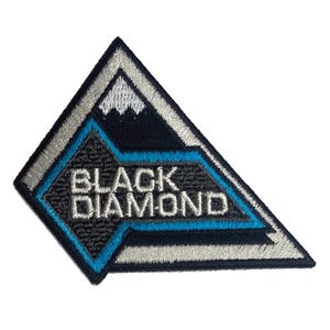 Peut inclure: Écusson brodé en forme triangulaire avec les mots "BLACK DIAMOND" en blanc. Le patch présente un motif de chaîne de montagnes en blanc et une forme de diamant bleu. La bordure est argentée.