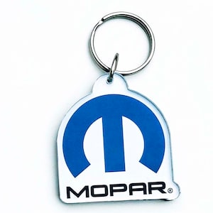 Könnte beinhalten: Ein blauer und weißer Mopar-Schlüsselanhänger mit einem silbernen Schlüsselring. Das Mopar-Logo ist ein blaues, stilisiertes M mit dem Wort Mopar in Schwarz darunter.