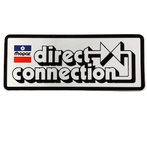 Pode incluir: Um adesivo retangular prateado e preto com o texto "direct connection" e um gráfico de seta estilizado. O adesivo também apresenta o logotipo da Mopar com o texto "Mopar" em azul e vermelho.