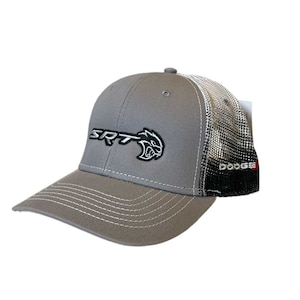 Puede incluir: Gorra de béisbol gris con el logotipo SRT y un gráfico de gato gruñón. La gorra tiene una parte trasera de malla y la palabra "DODGE" está impresa en el lateral. La visera y las costuras son blancas.