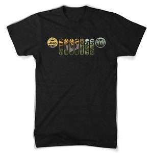 Könnte beinhalten: Schwarzes T-Shirt mit einem Grafikdruck einer Jeep-Kühlergrill mit Sonnenuntergang und Berglandschaft. Das Wort "Jeep" ist in einem gelben Kreis oben auf der Grafik geschrieben.