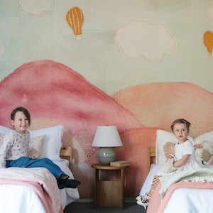May include: Two twin beds with pink and white bedding in a room with a mural of pink and orange mountains, clouds, and hot air balloons.