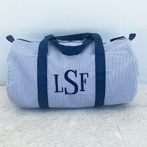 May include: A blue and white striped duffel bag with navy blue handles and a zipper closure. The bag has the monogram "LSF" embroidered on the front.