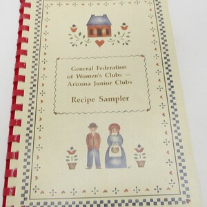 Könnte beinhalten: Ein Vintage-Kochbuch mit roter Spiralbindung. Der Umschlag zeigt eine handgezeichnete Illustration eines Hauses mit einem Herzen, Blumen und zwei Personen in traditioneller Kleidung. Der Titel lautet "General Federation of Women's Clubs - Arizona Junior Clubs Recipe Sampler".