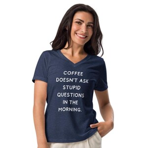 May include: A navy blue V-neck t-shirt with the text "COFFEE DOESN'T ASK STUPID QUESTIONS IN THE MORNING" in white. The shirt is made of a soft material.