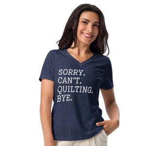 May include: Navy blue V-neck t-shirt with the text "SORRY. CAN'T. QUILTING. BYE." in white. The shirt is made of a soft material.