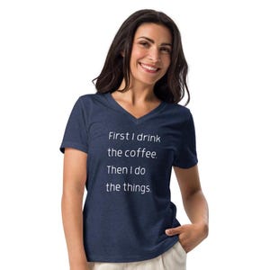 May include: A navy blue V-neck t-shirt with the text "First I drink the coffee. Then I do the things." in white. The shirt is made of a soft material.
