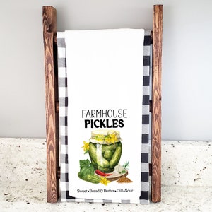 May include: White kitchen towel with a watercolor illustration of a jar of pickles. The text "FARMHOUSE PICKLES" is printed in black above the jar. The text "Sweet + Bread & Butter + Dill Sour" is printed in black below the jar.