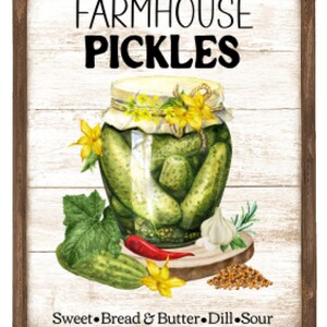 May include: A white sign with a brown wood frame features a watercolor illustration of a jar of pickles, garlic, mustard seeds, a red pepper, and a cucumber. The sign reads "Farmhouse Pickles" and "Sweet, Bread & Butter, Dill, Sour".