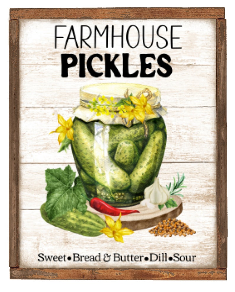 May include: A white sign with a brown wood frame features a watercolor illustration of a jar of pickles, garlic, mustard seeds, a red pepper, and a cucumber. The sign reads "Farmhouse Pickles" and "Sweet, Bread & Butter, Dill, Sour".