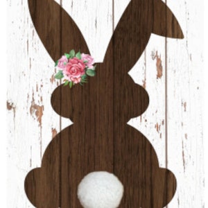 May include: A wooden bunny silhouette with a white fluffy tail and a floral arrangement on its head. The bunny is brown, set against a white, distressed wood background. The flowers are pink and red.
