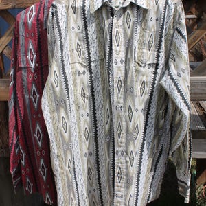 May include: Two long-sleeved button-down shirts hanging on a clothesline. One shirt is red with a white and black diamond pattern. The other shirt is tan, black, and white with a similar diamond pattern. Both shirts have buttoned pockets.