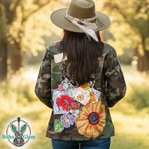 May include: A camouflage jacket with floral patches and a wide-brimmed hat. The back of the jacket features colorful, embroidered flowers and lace details. The hat is olive green with a feather and ribbon accent. The jacket is worn with blue jeans.