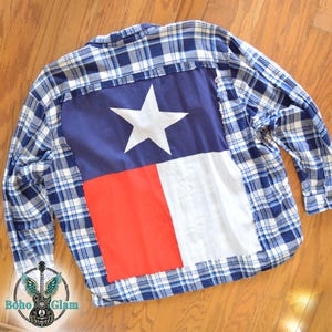 May include: Blue and white plaid shirt with a Texas flag design on the back. The flag features a white star on a blue background, with a red and white vertical stripe. The shirt is a button-down style.