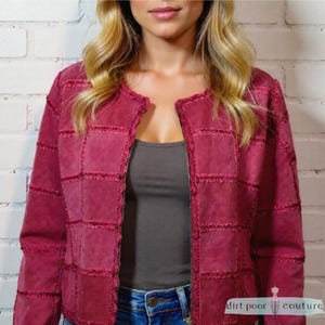 May include: A burgundy patchwork jacket with a round neckline and a zip fastening. The jacket is made of a soft material and has a textured appearance. The model is wearing a grey vest top and blue jeans. The jacket is from dirt poor couture.