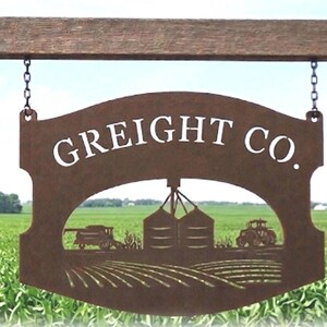 May include: A brown metal sign hanging from chains with the text GREIGHT CO. in white lettering. The sign features a cutout design depicting a farm scene with a combine harvester, grain silos, a tractor, and rows of crops in a field.