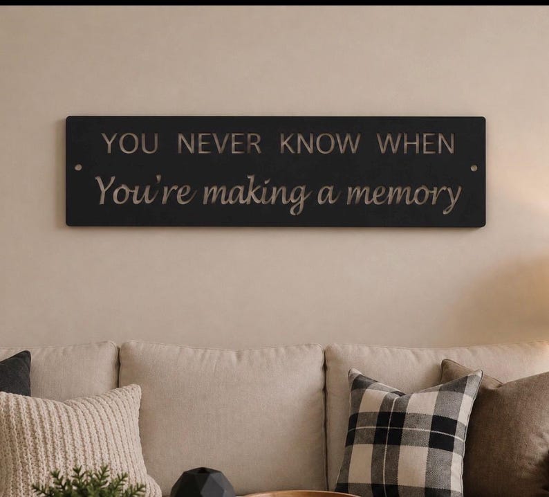 May include: A rectangular black wall sign featuring the engraved text "YOU NEVER KNOW WHEN You're making a memory" in a combination of uppercase and script fonts. The sign has a small circular hole on each side for mounting purposes.