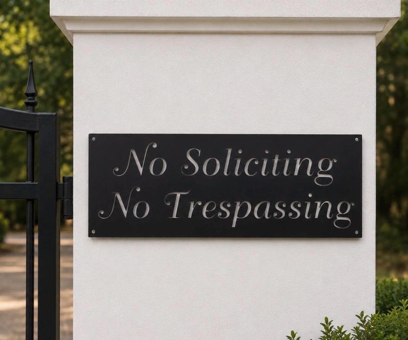 May include: A rectangular black metal sign mounted on a white pillar. The sign features cut-out lettering that reads No Soliciting and No Trespassing in a serif font. Four small silver screws secure the sign to the pillar at each corner.