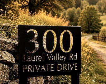 May include: A rectangular black metal sign featuring the house number 300 in large, bold, metallic-toned numerals. Below the number, the text reads Laurel Valley Rd and PRIVATE DRIVE in a clean, sans-serif font with a metallic finish.