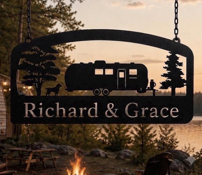 Puede incluir: Un letrero colgante de metal negro con la silueta de una caravana, un perro y dos &aacute;rboles. El texto "Richard & Grace" est&aacute; recortado en la parte inferior del letrero. El letrero est&aacute; suspendido por dos cadenas de metal en las esquinas.