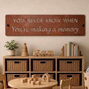 May include: A rectangular, rust-colored metal wall sign featuring the laser-cut text "YOU NEVER KNOW WHEN You're making a memory" in a combination of block and script fonts, mounted with two black circular fasteners on the left and right sides.