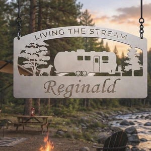 Puede incluir: Un letrero colgante de metal rectangular con un dise&ntilde;o cortado con l&aacute;ser de una caravana, un perro y dos &aacute;rboles. El texto "LIVING THE STREAM" est&aacute; arqueado en la parte superior y el nombre "Reginald" est&aacute; cortado en letra cursiva.
