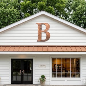May include: Exterior view of a white building with a large, copper-colored letter "B" mounted on the gable. The building has a copper-colored roof and a black double door entrance. A sign reads "EST. 1928".