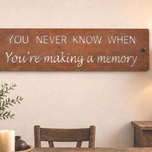 May include: A rectangular metal wall sign with a rusted brown finish featuring the cut-out text "YOU NEVER KNOW WHEN" in block letters and "You're making a memory" in a cursive script, secured by two dark circular fasteners on the left and right.