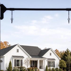 May include: A black metal sign post featuring a vertical pole and a horizontal arm extending outwards. The horizontal arm includes two hanging hooks with circular loops at the bottom, designed for suspending a sign in an outdoor setting.
