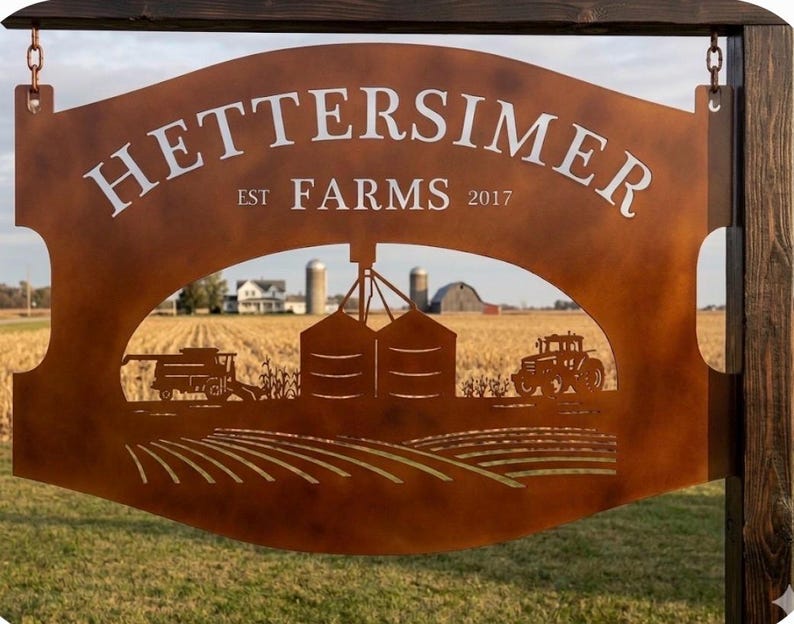 May include: A rust-colored metal sign featuring the text HETTERSIMER FARMS EST 2017. The sign has a cutout design depicting a farm scene with a combine harvester, grain silos, a tractor, and rows of crops, suspended by chains from a wooden post.